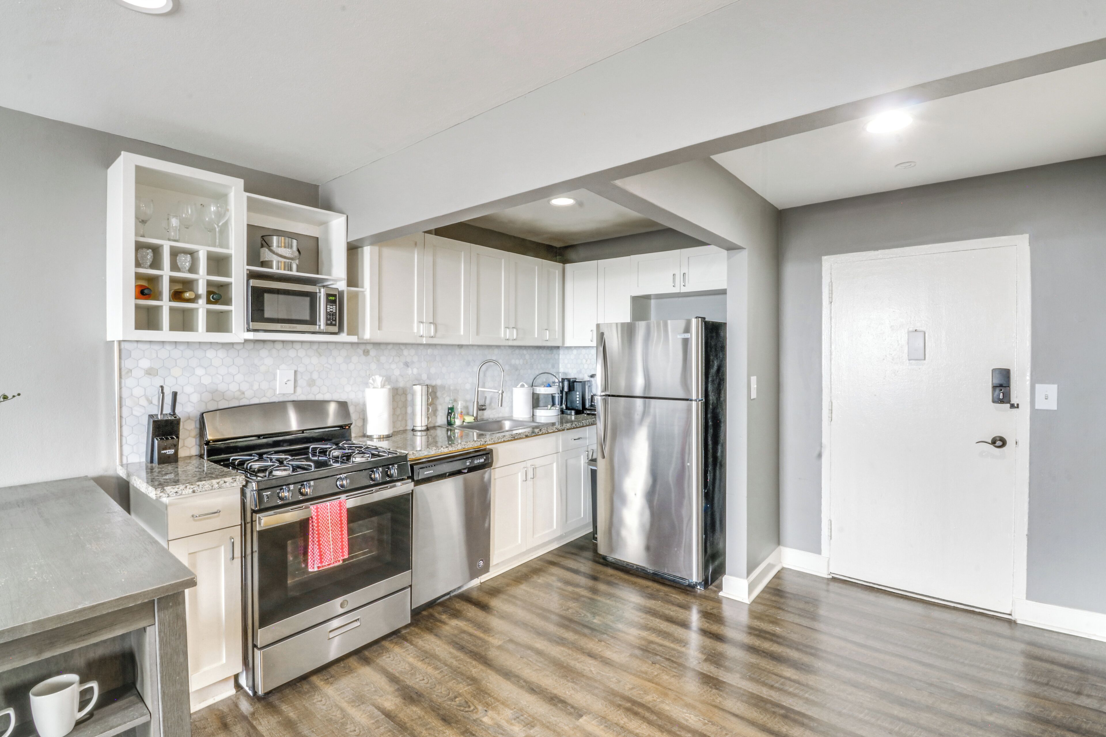 A modern kitchen with stainless steel appliances, white cabinetry, and a wooden floor.