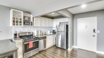 A modern kitchen with stainless steel appliances, white cabinetry, and a wooden floor.