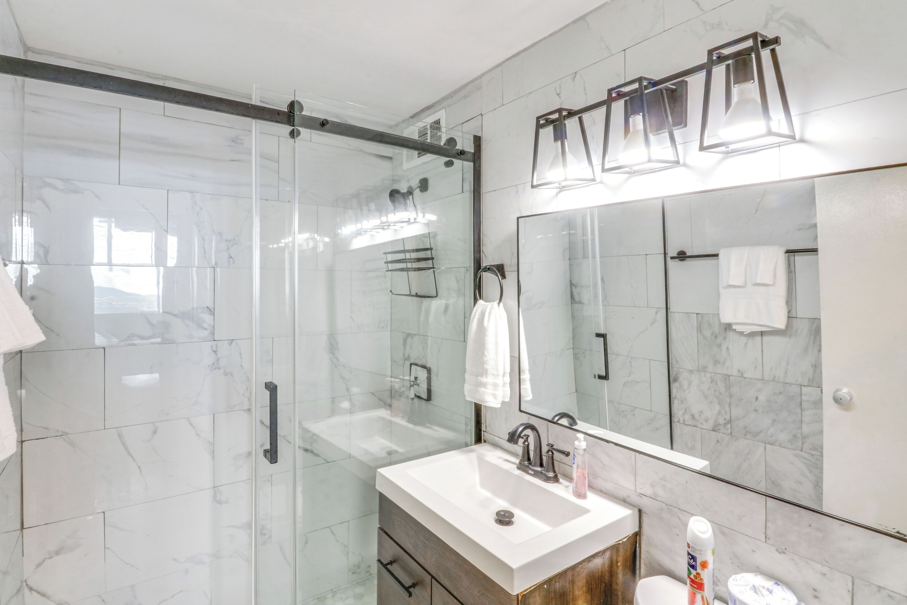 A modern bathroom with a glass-enclosed shower, a large mirror, and a white sink.