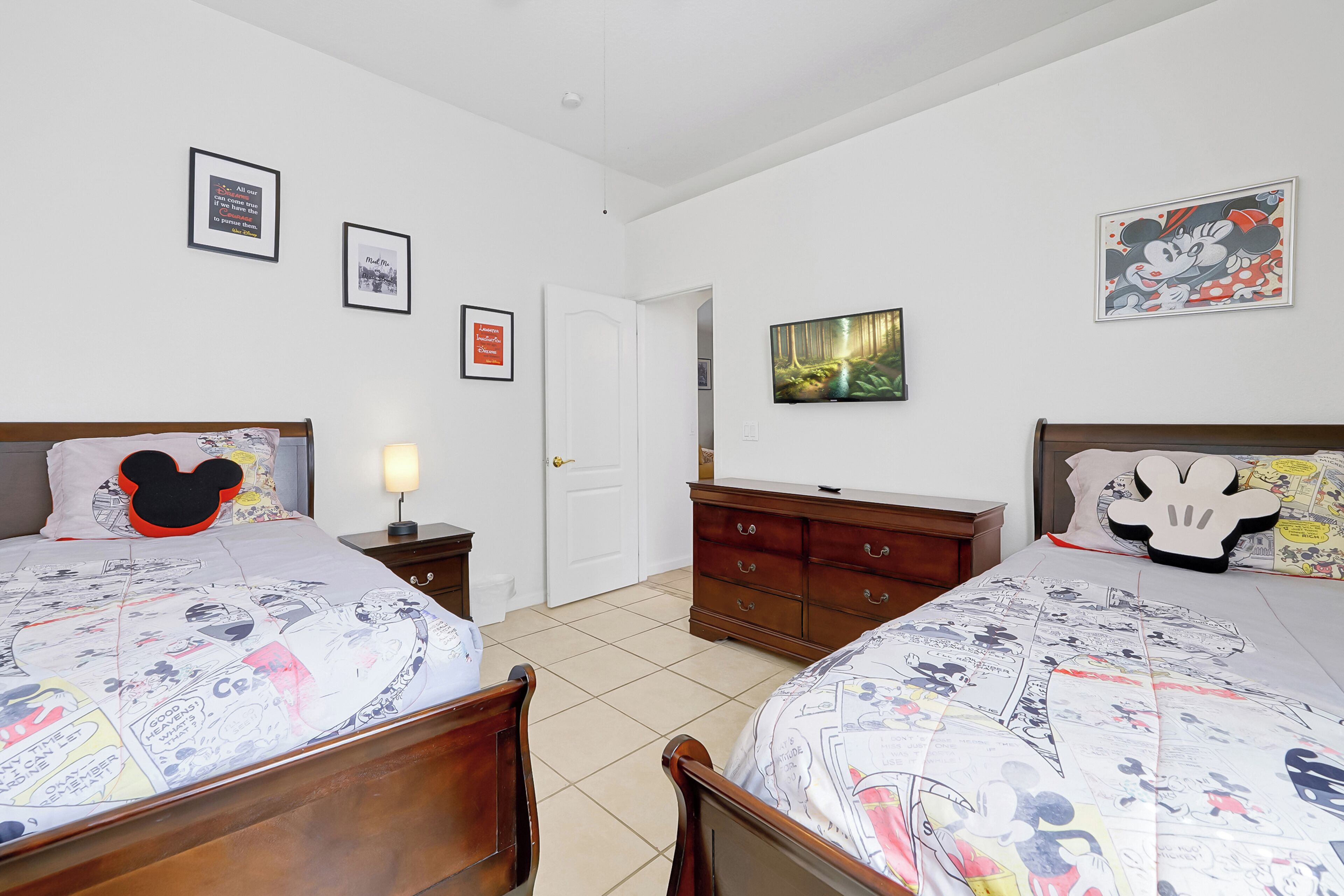 A bedroom with two beds, a dresser, a nightstand, a lamp, and framed pictures on the walls.