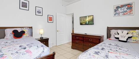 A bedroom with two beds, a dresser, a nightstand, a lamp, and framed pictures on the walls.