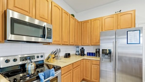 A modern kitchen with stainless steel appliances, wooden cabinets, and a tiled backsplash. - 4BR Golf Villa w/ Pool, Near Disney & Beaches (Davenport)