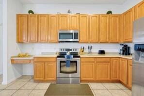 A modern kitchen with wooden cabinets, stainless steel appliances, and a tiled floor. - 4BR Golf Villa w/ Pool, Near Disney & Beaches (Davenport)