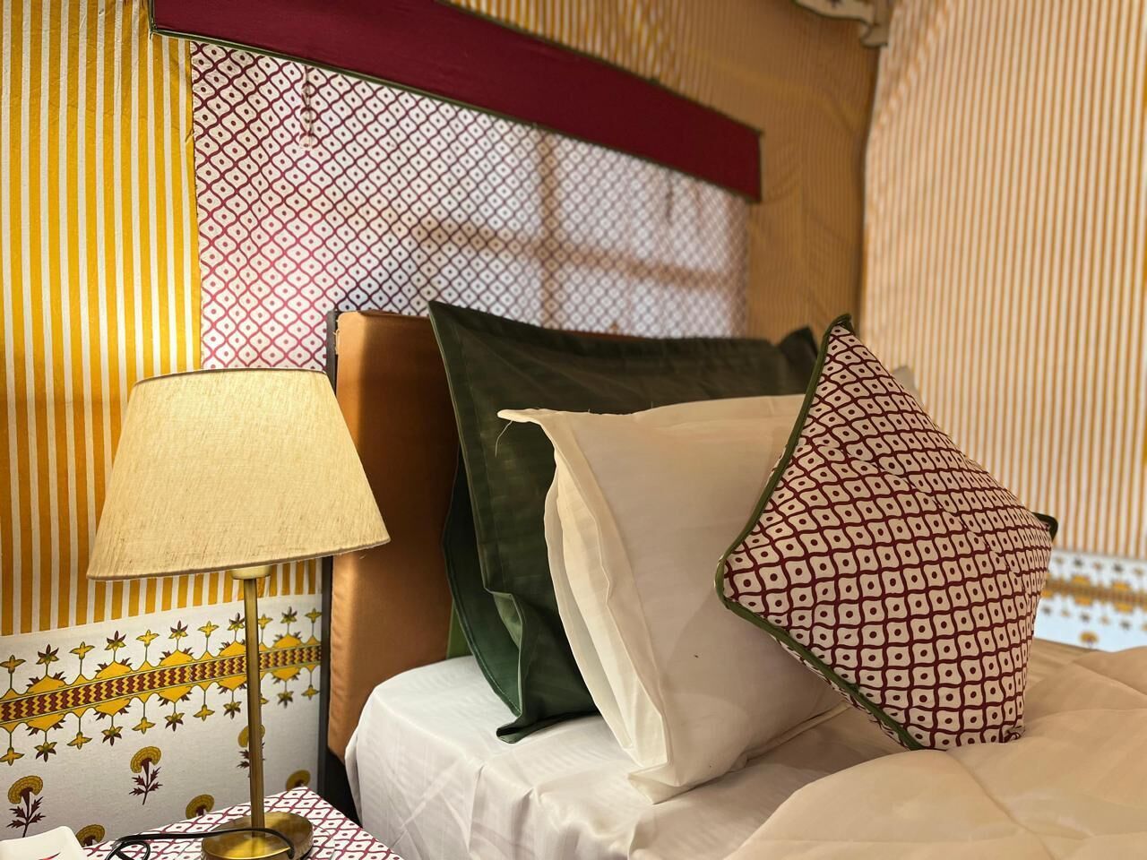 Ein Hotelzimmer mit Bett, Kissen, einer Lampe und gemusterten Vorhängen.