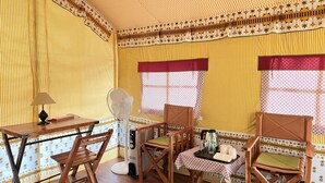 A room with a wooden table, two chairs, a standing fan, and a small table with a tray.