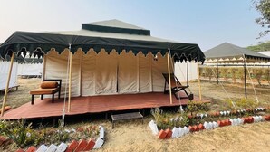 A tent with a platform and seating area, surrounded by a landscaped garden.
