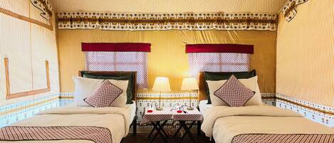 A room with two beds, a small table with lamps, and patterned curtains.