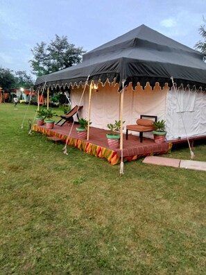 Una gran carpa con una plataforma y una zona de estar, rodeada de césped.