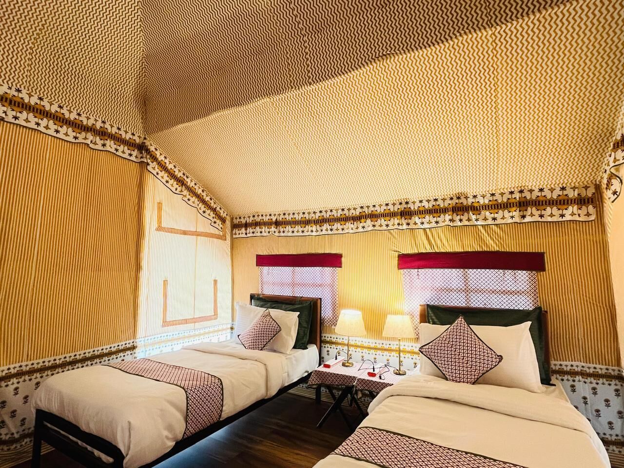 A room with two beds, a patterned ceiling, and a window with a red valance.