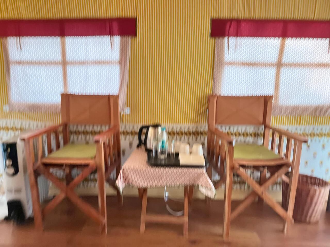 A small table with a checkered tablecloth, two wooden chairs with cushions, and a kettle on the table.