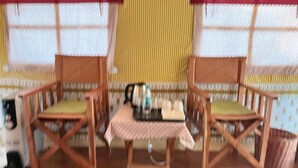 A small table with a checkered tablecloth, two wooden chairs with cushions, and a kettle on the table.