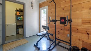 A home gym with a pull-up bar and weight bench, a wooden wall, and a door leading to a kitchen area. - Mid-term Stay in Austin! Family Home w/ Backyard (Austin)
