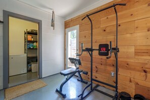 A home gym with a pull-up bar and weight bench, a wooden wall, and a door leading to a kitchen area. - Mid-term Stay in Austin! Family Home w/ Backyard (Austin)