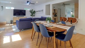 A modern living room with a sectional sofa, dining table with chairs, a flat-screen TV, ceiling fans, and a large window. - Mid-term Stay in Austin! Family Home w/ Backyard (Austin)