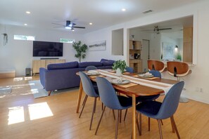 A modern living room with a sectional sofa, dining table with chairs, a flat-screen TV, ceiling fans, and a large window. - Mid-term Stay in Austin! Family Home w/ Backyard (Austin)