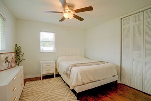 Een slaapkamer met een bed, nachtkastje, dressoir, plafondventilator, raam en garderobe.