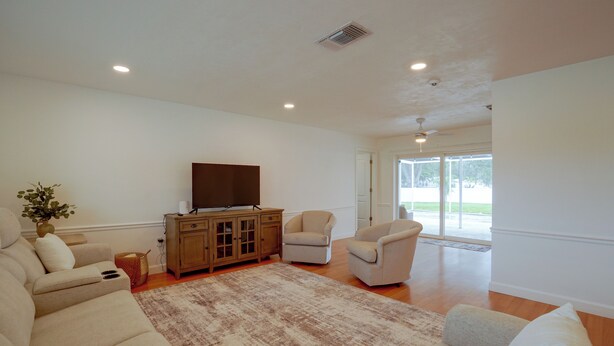 A living room with a beige sofa, a television on a wooden cabinet, and a large window with a view of the outdoors. - Lanai, Golf Views! Extended Sarasota Stay (Sarasota)
