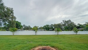 A grassy yard with a circular stone fire pit in the foreground. - Lanai, Golf Views! Extended Sarasota Stay (Sarasota)