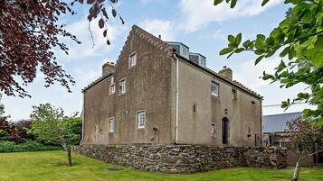 A stone building with a sloped roof, a small garden, and a clear sky.