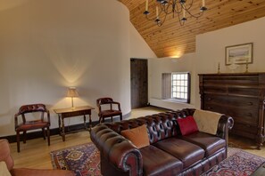 A spacious living room with a leather sofa, wooden chairs, a table with a lamp, and a large window. - Historic 3‑bedroom, 3‑bathroom Highland castle near Portmahomack. (Portmahomack)