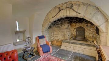 Una habitació acollidora amb una llar de pedra, un sofà de cuir vermell, una taula petita amb llibres i una estoreta amb dibuixos.