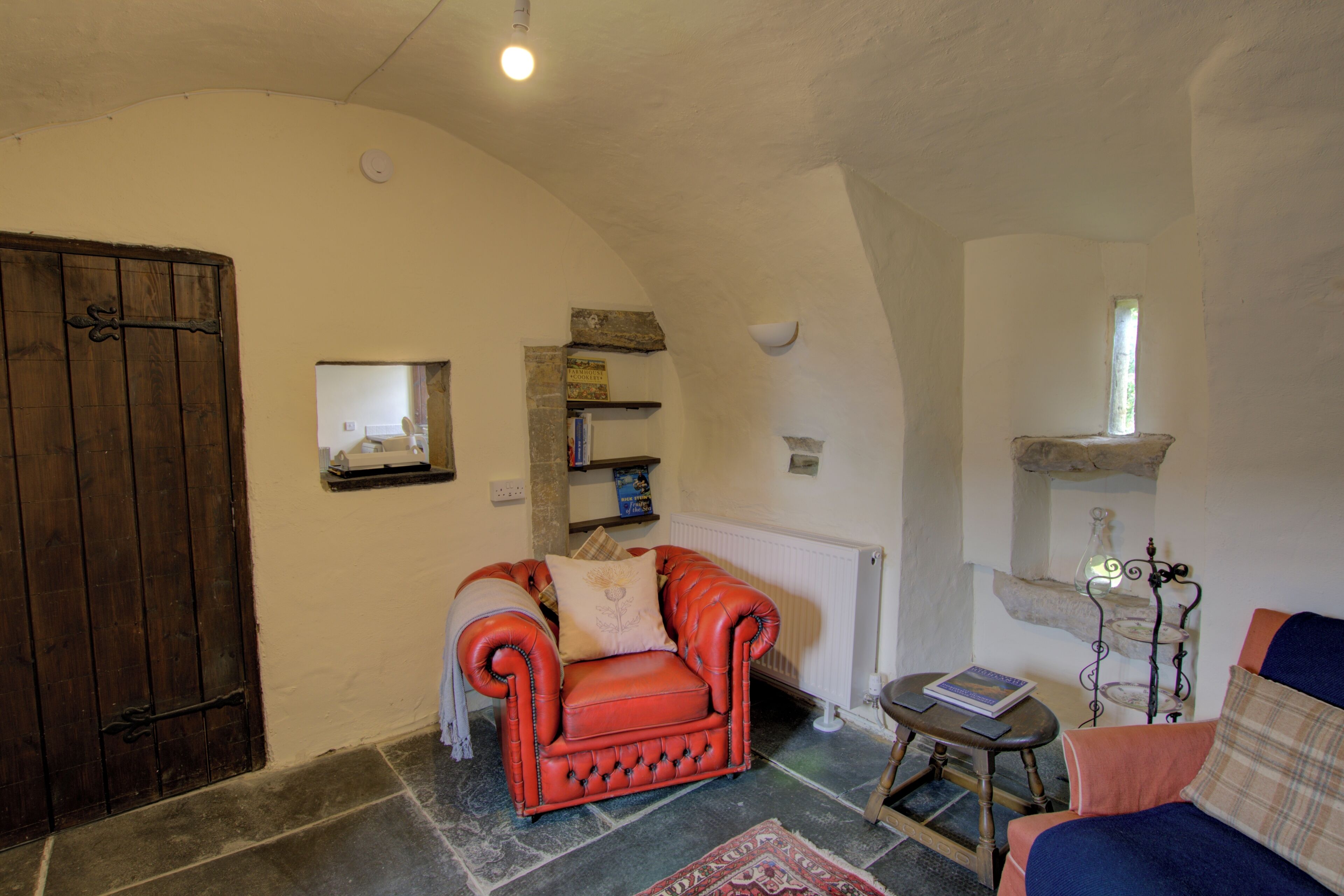 Une pièce chaleureuse avec un fauteuil rouge, une petite table sur laquelle repose un livre, une cheminée et un mur en pierre.