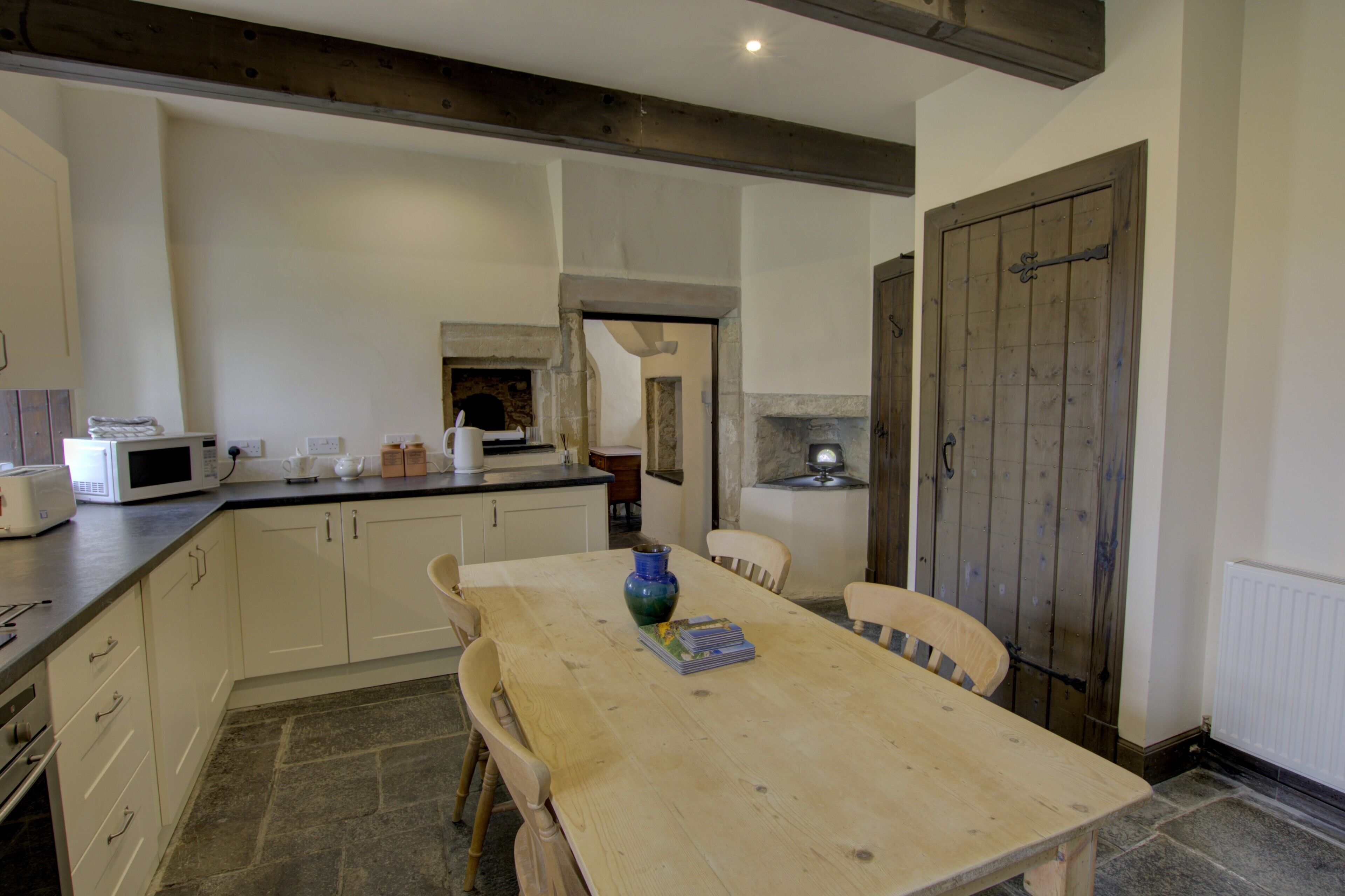 A kitchen with a wooden table, chairs, a microwave, and a stone fireplace.