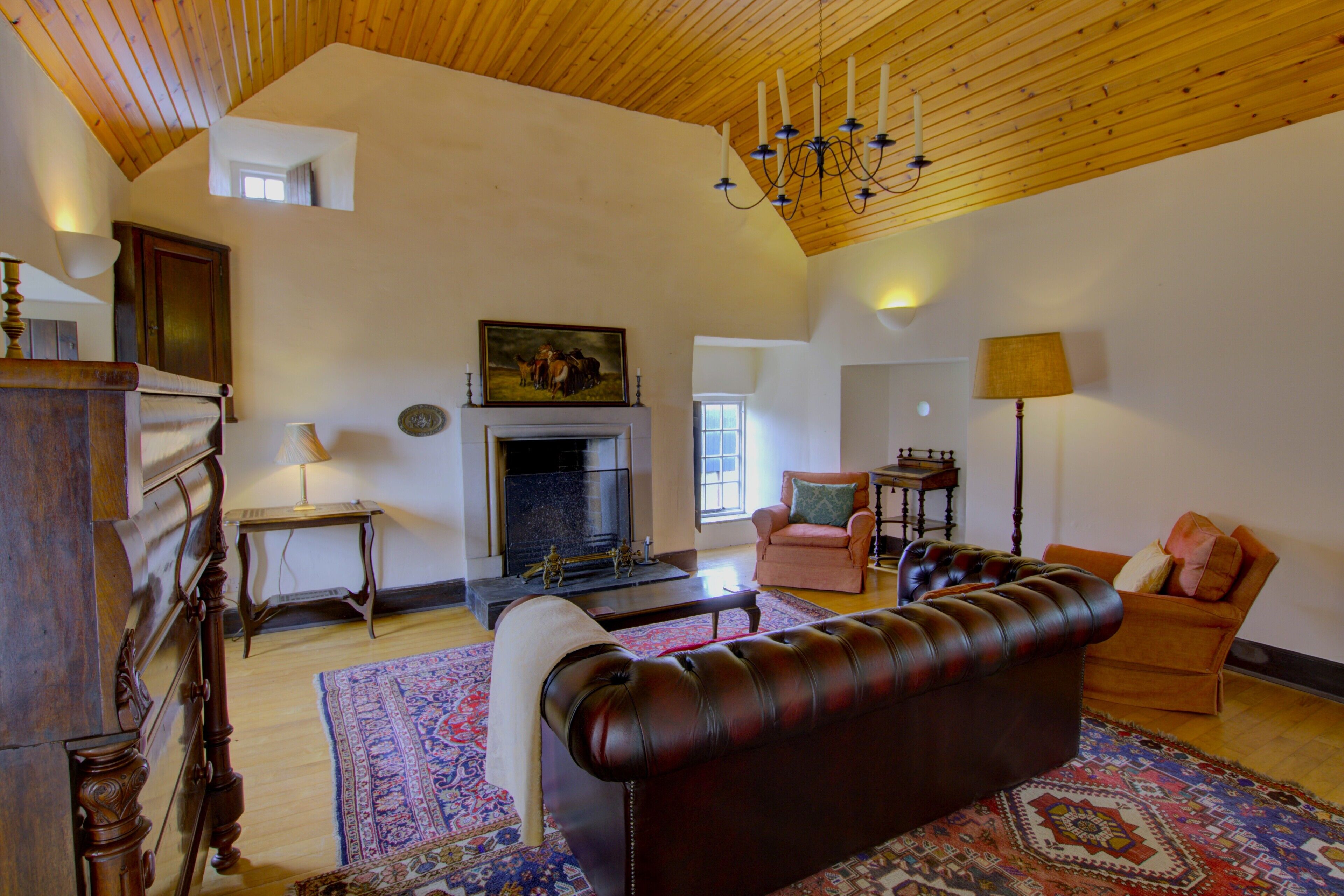 A spacious living room with a fireplace, leather sofa, and a chandelier.