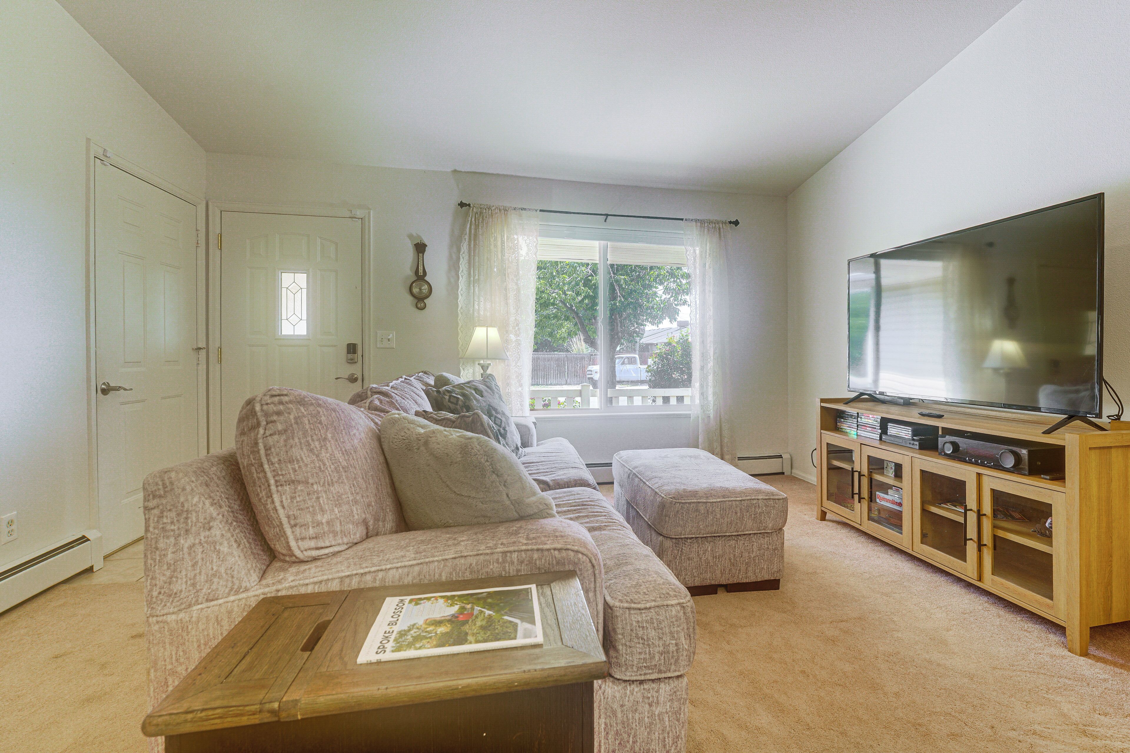 A living room with a sectional sofa, a coffee table, a television on a wooden stand, and a window with curtains.