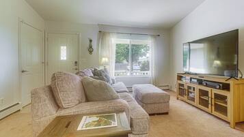A living room with a sectional sofa, a coffee table, a television on a wooden stand, and a window with curtains.