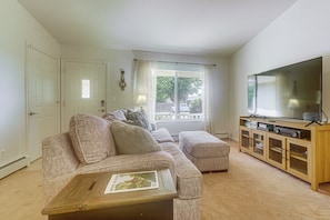 A living room with a sectional sofa, a coffee table, a television on a wooden stand, and a window with curtains. - Grand Junction Home w/ Patio: Shop, Dine & Hike! (Grand Junction)