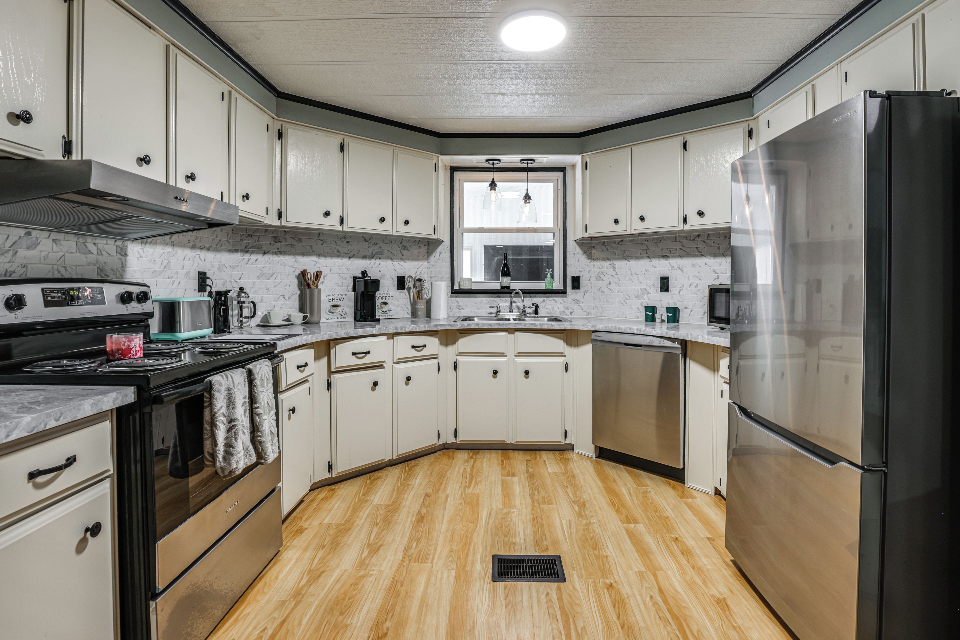 A kitchen with white cabinets, a stainless steel refrigerator, a stove, and a window above the sink.