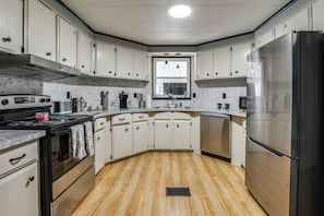 A kitchen with white cabinets, a stainless steel refrigerator, a stove, and a window above the sink. - 4-passenger Golf Cart! Fun in the Villages (Lady Lake)