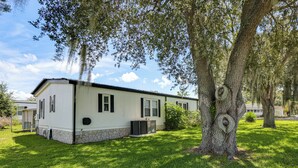 Ein Bungalow mit Stein Fundament, einer kleinen angebauten Garage und einem Rasen mit Bäumen.