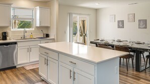Una cocina moderna con armarios blancos, una isla central y un comedor con una mesa preparada para cuatro.
