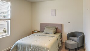 Un dormitorio con cama, una silla, una mesita de noche y una ventana con persianas.