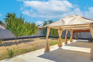 Un espace extérieur abrité, doté d’un sol en béton, entouré d’une clôture en bois et d’arbres.