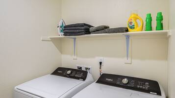 A laundry area with two front-loading washers, a shelf with folded towels and laundry supplies, and a power outlet.
