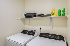 A laundry area with two front-loading washers, a shelf with folded towels and laundry supplies, and a power outlet.