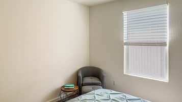 A bedroom with a bed, a chair, a small table, and a window with blinds.