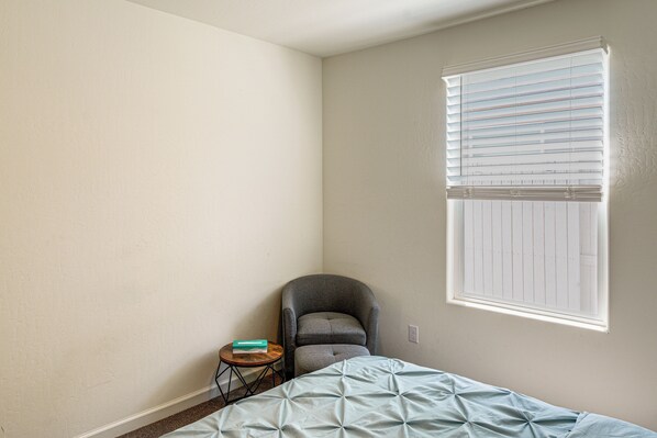 A bedroom with a bed, a chair, a small table, and a window with blinds.