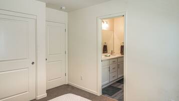 A hallway with a white carpet, a door, and a bathroom with a mirror, sink, and towel rack.