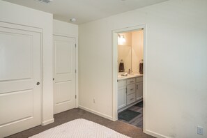A hallway with a white carpet, a door, and a bathroom with a mirror, sink, and towel rack.