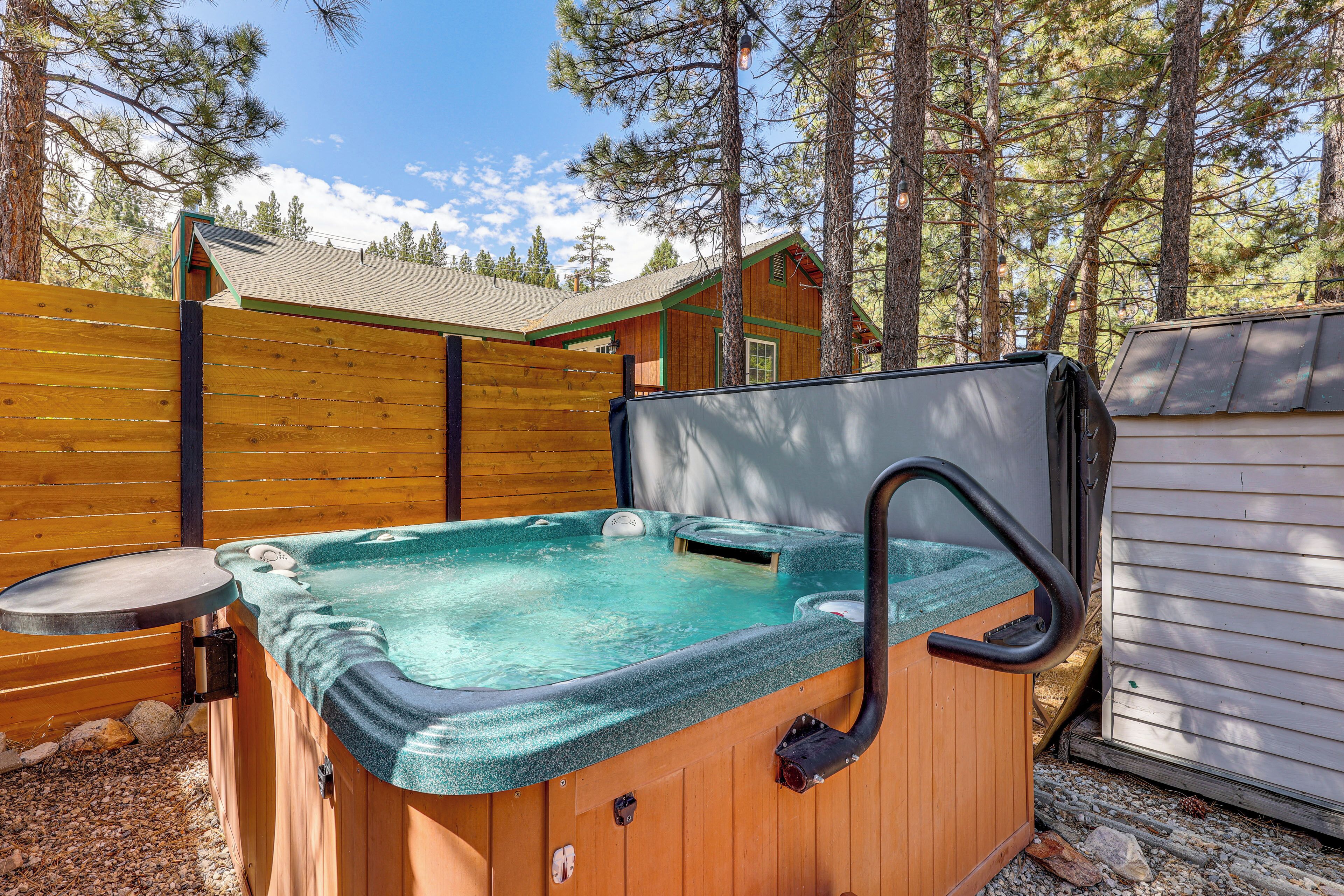 A wooden hot tub with a built-in seat and a single faucet, surrounded by a wooden fence and a house in the background.