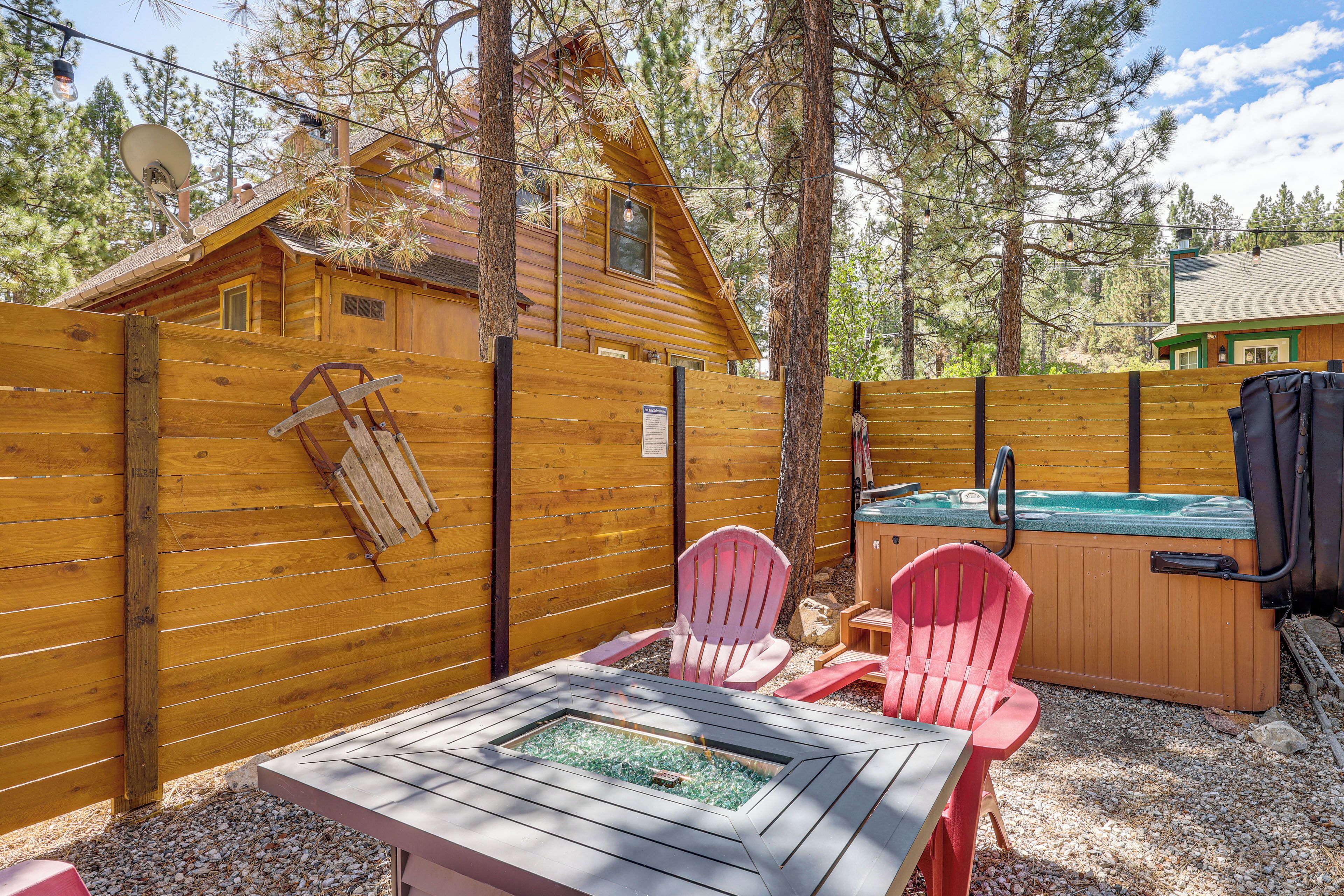 Eine Holzhütte mit Whirlpool, zwei Adirondack-Stühlen und einer Feuerstelle.
