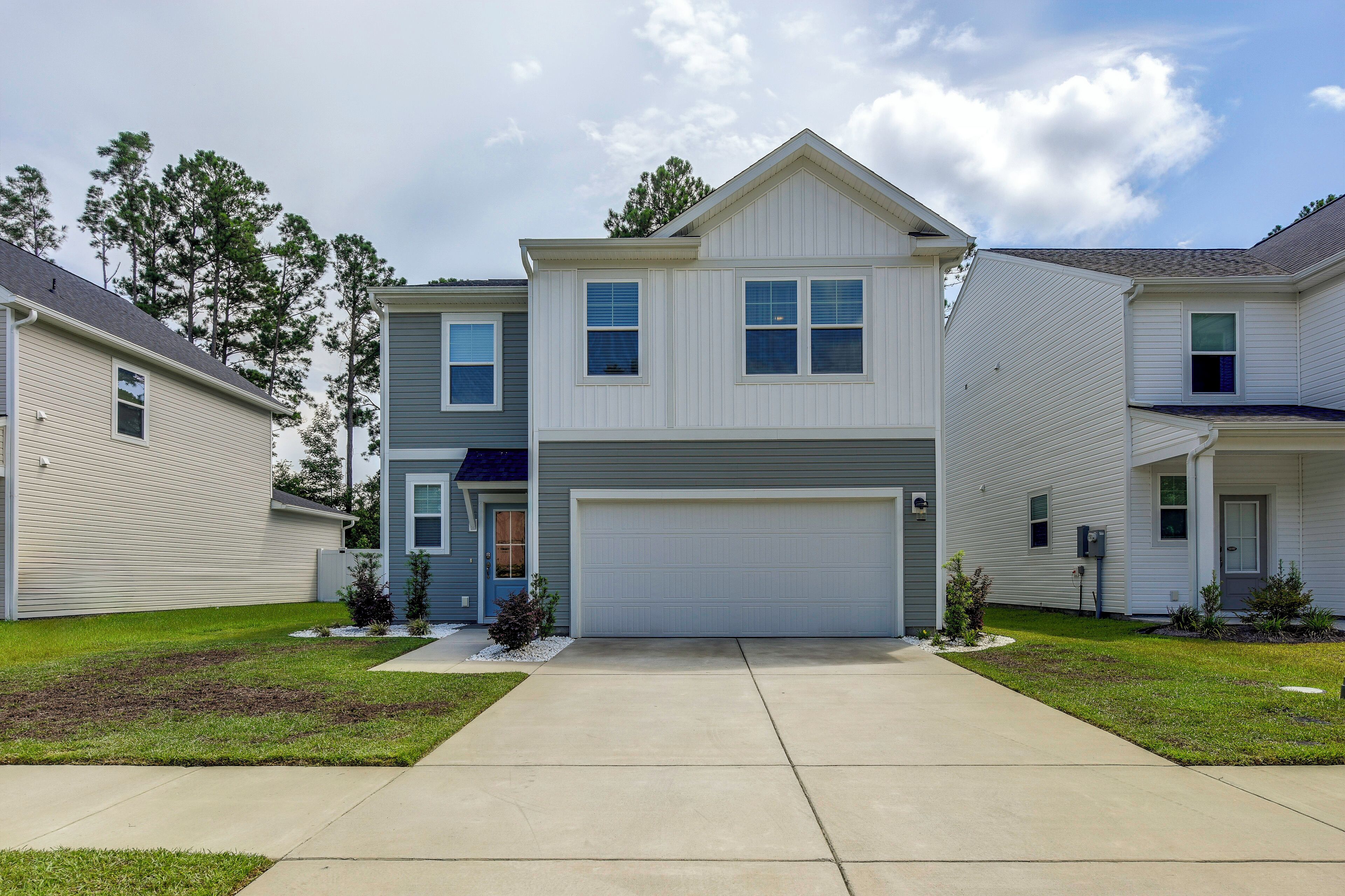 A two-story residential building with a central garage door, a front entrance with a blue door, and a small front yard with landscaping.
