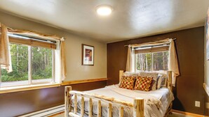 A bedroom with a wooden bed, two windows with curtains, a framed picture on the wall, and a ceiling light. - Pool Table & Peaceful Porch: Fairplay Retreat (Fairplay)