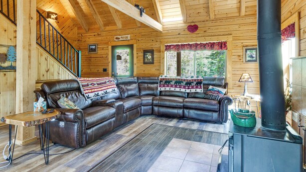 A cozy cabin interior with a leather sectional sofa, a fireplace, wooden walls, and a staircase. - Pool Table & Peaceful Porch: Fairplay Retreat (Fairplay)