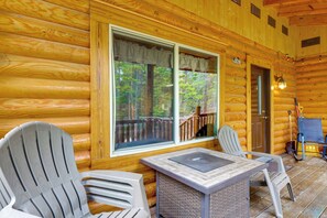 Eine Blockhütte mit zwei Adirondack-Stühlen, einem Tisch und einer Tür, die auf eine Veranda führt.