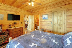 Ein Holzblockbau-Innenraum mit Bett, Kommode, Fernseher und Deckenventilator.